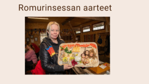 Vaaleatukkainen nainen seisoo esittelemässä taideteosta, jossa on kukkia, pitsiä ja nukenpäitä.