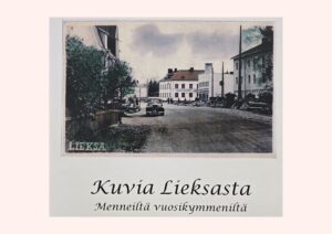 Kuvassa on vanha valokuva kaupunkinäkymästä. Kuvassa on katu, jonka molemmin puolin on rakennuksia. Kadulla on auto ja henkilöitä. Teksti: Kuvia Lieksasta Menneiltä vuosikymmeniltä